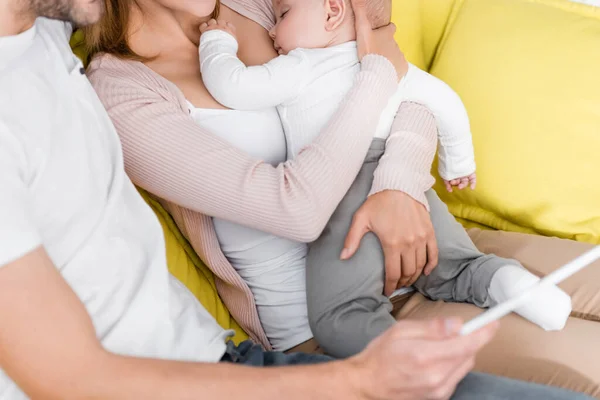 Uomo con tablet digitale vicino moglie in braccio sonnolento figlio neonato — Foto stock