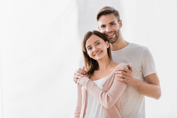 Homem feliz abraçando esposa alegre e olhando para a câmera — Fotografia de Stock