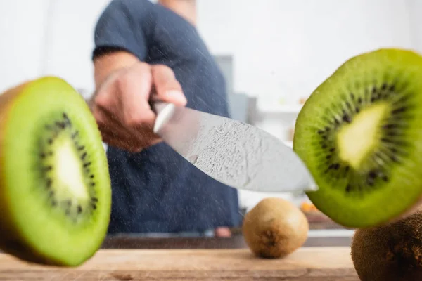 Vue rapprochée des moitiés de kiwis près du couteau en main de l'homme sur fond flou — Photo de stock