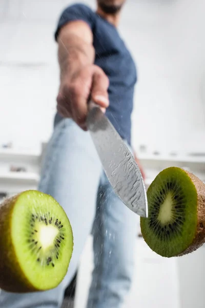 Close up view of wet knife near halves of juicy kiwi with man on blurred background - foto de stock