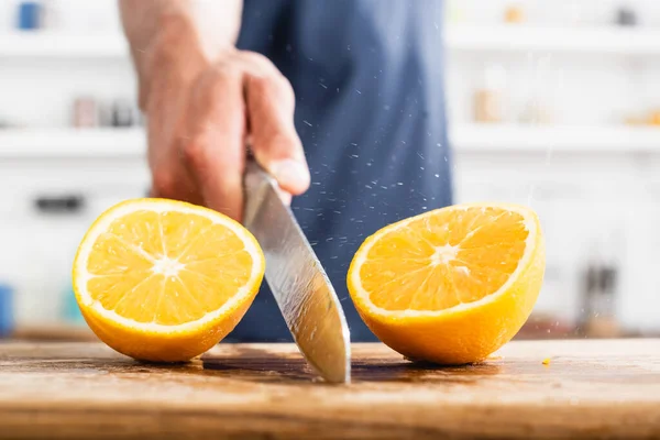 Close-up vista de metades de laranja suculenta e faca molhada na mão do homem no fundo borrado — Fotografia de Stock