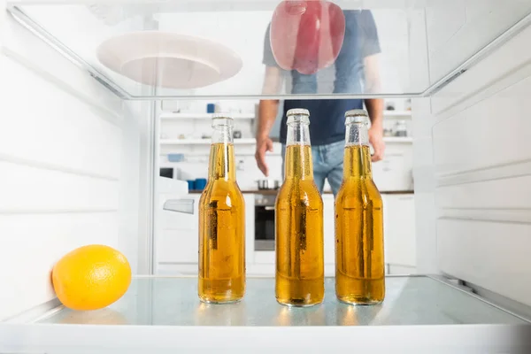Bottles of beer and orange in fridge near man on blurred background — Stock Photo