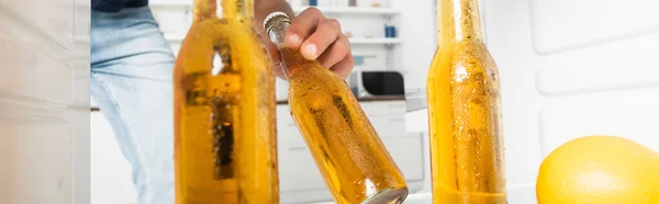 Vista ritagliata dell'uomo che prende una bottiglia di birra bagnata dal frigorifero aperto su sfondo sfocato, banner — Foto stock