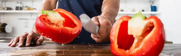 Cropped view of man holding knife near halves of paprika on blurred foreground, banner — Stock Photo