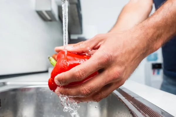 Close up view of man washing bell pepper in kitchen - foto de stock