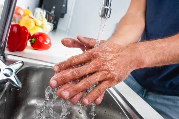 Vue recadrée de l'homme se lavant les mains dans la cuisine près des légumes sur fond flou — Photo de stock