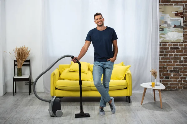 Smiling man standing near vacuum cleaner in living room — Stock Photo