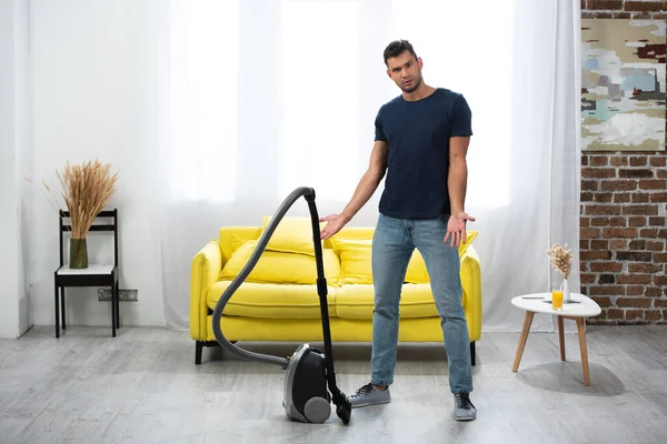 Young man pointing with hands near vacuum cleaner in living room — Stock Photo