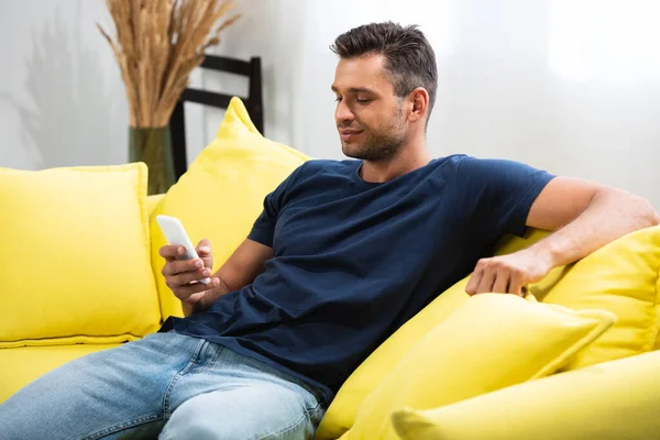 Homem usando smartphone enquanto sentado no sofá na sala de estar — Fotografia de Stock