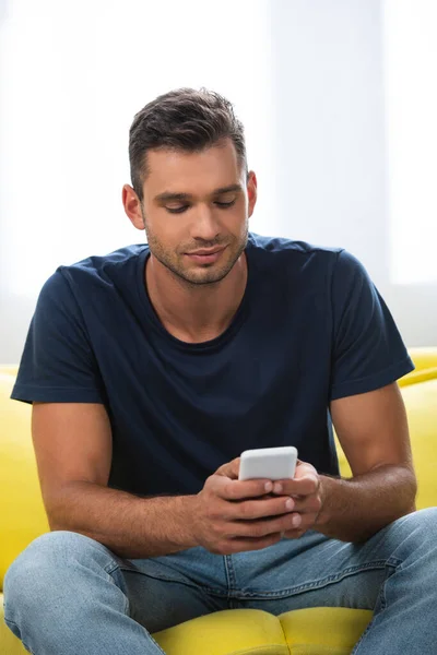 Young man in casual clothes using smartphone on couch at home — Stock Photo