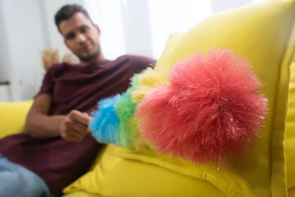 Spazzola di polvere colorata in mano del giovane su sfondo sfocato sul divano — Foto stock