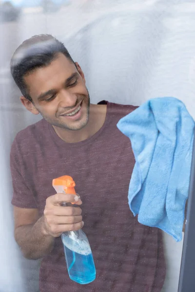 Homme souriant nettoyage verre de fenêtre avec détergent et chiffon — Photo de stock