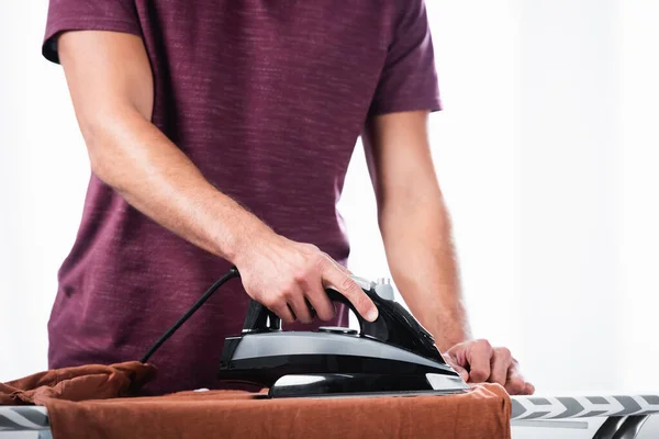 Cropped view of young man ironing clothes on board at home - foto de stock