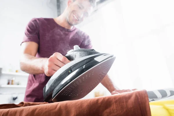 Iron with steam near clothes in hand of smiling man on blurred background — Stock Photo