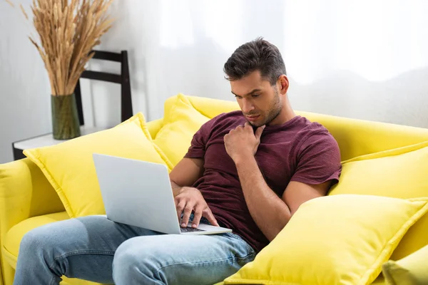 Pensive freelancer using laptop on sofa at home — Stock Photo