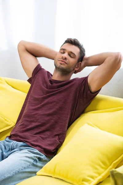 Young man with hands near head resting on couch at home - foto de stock