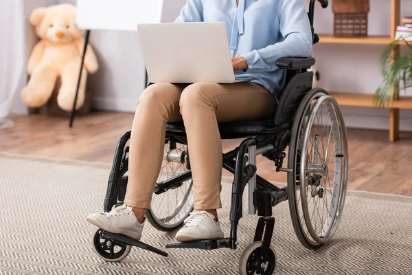 Vista recortada del psicólogo que utiliza el ordenador portátil mientras está sentado en silla de ruedas con la oficina borrosa en el fondo - foto de stock