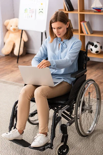 Longitud completa de psicólogo usando el ordenador portátil mientras está sentado en silla de ruedas en la oficina - foto de stock