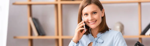 Joyeuse psychologue féminine regardant la caméra tout en parlant sur un téléphone mobile sur fond flou, bannière — Photo de stock