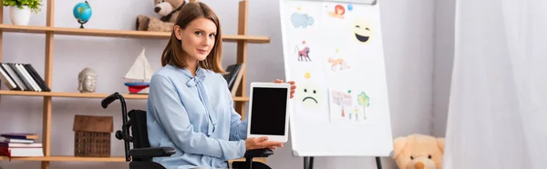 Female psychologist showing digital tablet with blank screen while sitting in wheelchair in office, banner — Stock Photo