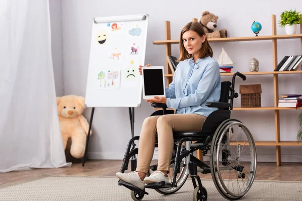 Longitud completa de la psicóloga femenina mostrando tableta digital mientras está sentada en silla de ruedas en la oficina - foto de stock