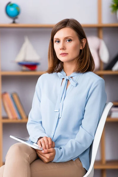 Female psychologist with digital tablet looking at camera while sitting on chair on blurred background — Stock Photo