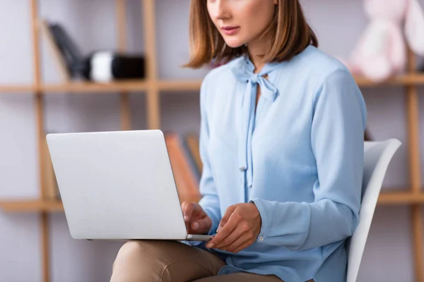 Vista cortada do psicólogo feminino usando laptop enquanto sentado na cadeira em fundo embaçado — Fotografia de Stock