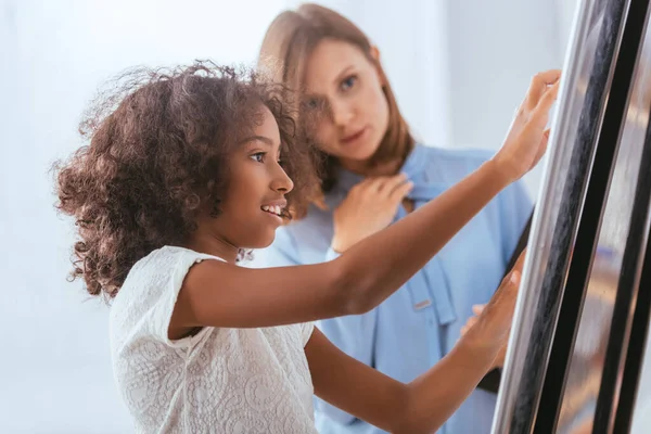 Smiling african american girl near whiteboard with blurred psychologist on background — Stock Photo
