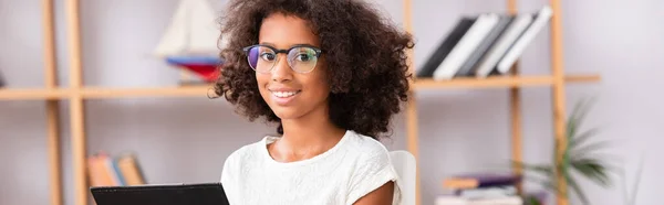 Portrait of african american girl in eyeglasses looking at camera on blurred background, banner — Stock Photo