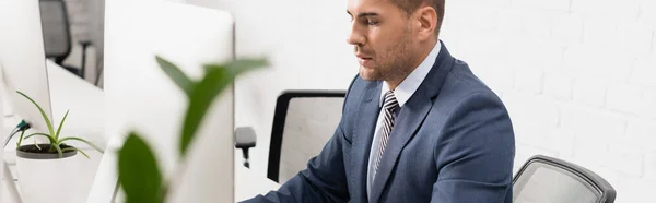 Focused executive sitting near computer monitor at workplace on blurred foreground, banner — Stock Photo