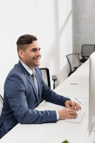 Lächelnder Geschäftsmann tippt auf Computertastatur, während er am Arbeitsplatz im Büro sitzt — Stockfoto