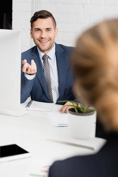 Alegre hombre de negocios gesto, mientras se sienta a la mesa con una compañera borrosa en primer plano - foto de stock