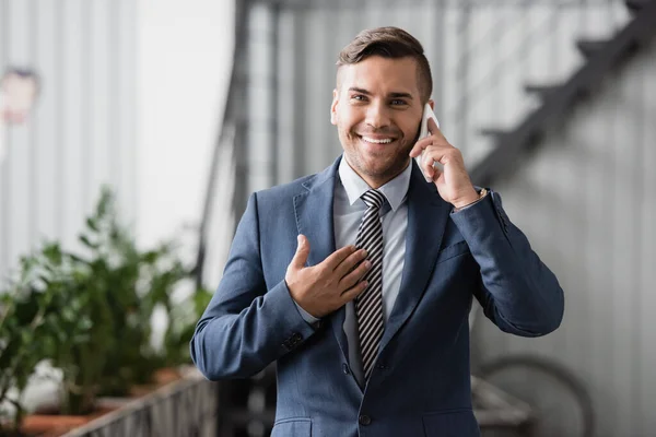 Smiling executive looking at camera, while talking on mobile phone at work on blurred background — Stock Photo