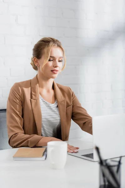 Executiva mulher sentada no local de trabalho com laptop no escritório em primeiro plano desfocado — Fotografia de Stock