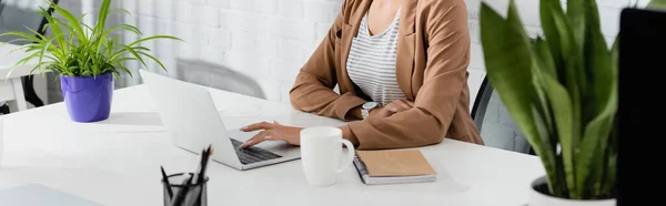 Vista recortada de la ejecutiva femenina usando el ordenador portátil, mientras está sentado en el lugar de trabajo en primer plano borroso, pancarta - foto de stock