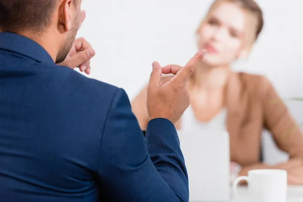 Rückansicht des Geschäftsmannes, der mit dem Finger auf verschwommene Kollegin im Hintergrund zeigt — Stockfoto