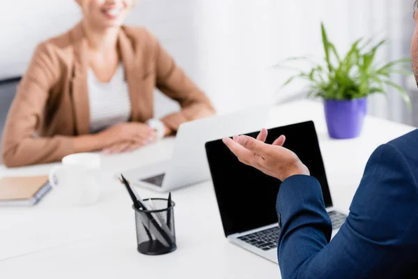 Ausgeschnittene Ansicht eines Geschäftsmannes gestikulierend, während er mit Laptop auf verschwommenem Hintergrund am Arbeitsplatz sitzt — Stockfoto