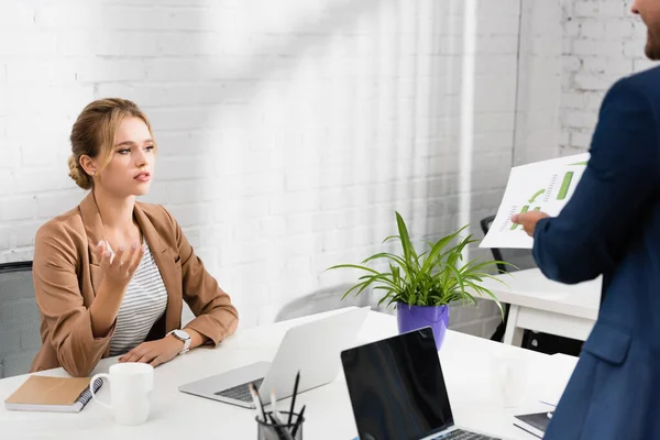 Weibliche Führungskraft gestikuliert, während sie das Dokument in den Händen eines Mitarbeiters betrachtet, der in der Nähe seines Arbeitsplatzes steht — Stock Photo