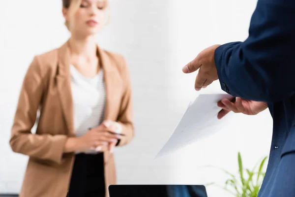 Vista recortada del hombre de negocios con documentos gesticulados con una compañera borrosa sobre el fondo - foto de stock