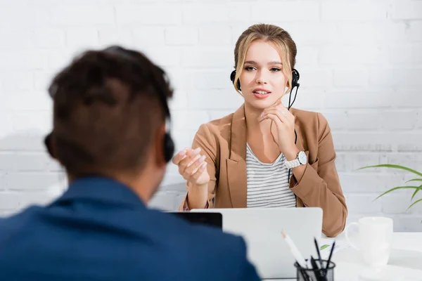 Consultante en gestuelle de casque, assise sur le lieu de travail, au premier plan flou — Photo de stock