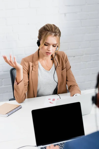 Consultora no gesto dos auscultadores, sentada à mesa no escritório em primeiro plano desfocado — Fotografia de Stock