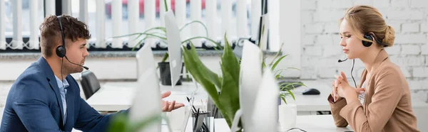 Operatori di call center in cuffie funzionanti, seduti a tavola su primo piano sfocato, banner — Foto stock