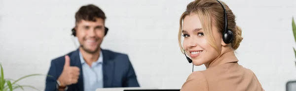 Lächelnde Bedienerin im Headset mit verschwommenem Kollegen im Hintergrund, Banner — Stockfoto