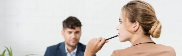 Ejecutivo femenino reflexivo con pluma, mirando hacia otro lado con compañero borroso en el fondo, bandera - foto de stock