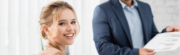 Mujer feliz ejecutivo mirando a la cámara con borrosa compañero de trabajo en el fondo, pancarta - foto de stock