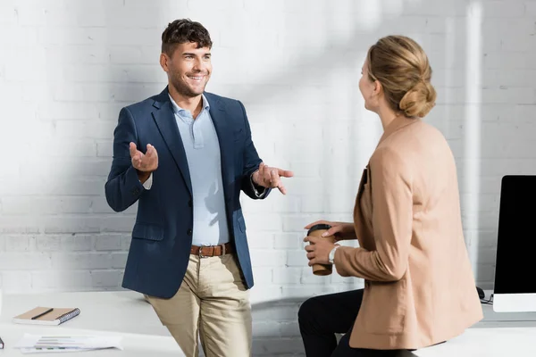 Gestor de empresário sorridente, enquanto conversa com colega perto do local de trabalho durante a pausa no escritório — Fotografia de Stock