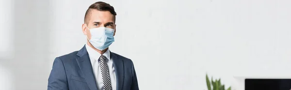 Businessman in medical mask looking away on blurred background, banner — Stock Photo