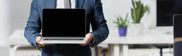 Обрізаний вид виконавчої влади в формальному одязі, що показує ноутбук з порожнім екраном з розмитим офісом на фоні, банер — стокове фото