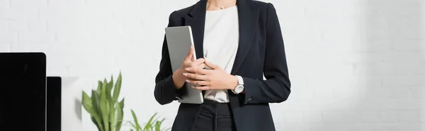 Cropped view of businesswoman in formal wear holding laptop near plants and computer monitors, banner — Stock Photo