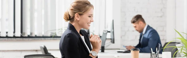 Femme d'affaires heureuse regardant ordinateur portable, tout en étant assis sur le lieu de travail sur fond flou, bannière — Photo de stock